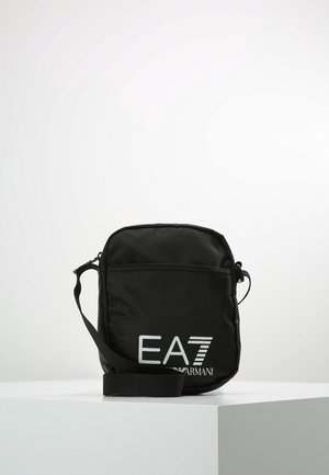 Sac bandoulière compact noir avec sangle réglable, poche avant, et logo blanc EA7 Emporio Armani sur le devant sur fond uni.