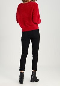Czerwony, puszysty, dziany sweter z okrągłym dekoltem, zestawiony z czarnymi obcisłymi jeansami i czarnymi botkami za kostkę. Miękka faktura i luźny krój.