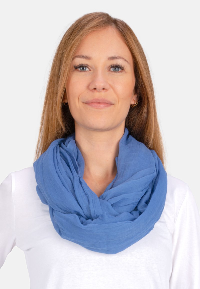 Écharpe infinie bleue, légère, faite de tissu texturé, drapée en boucles. Portée sur un haut blanc, affichant une apparence douce et décontractée.