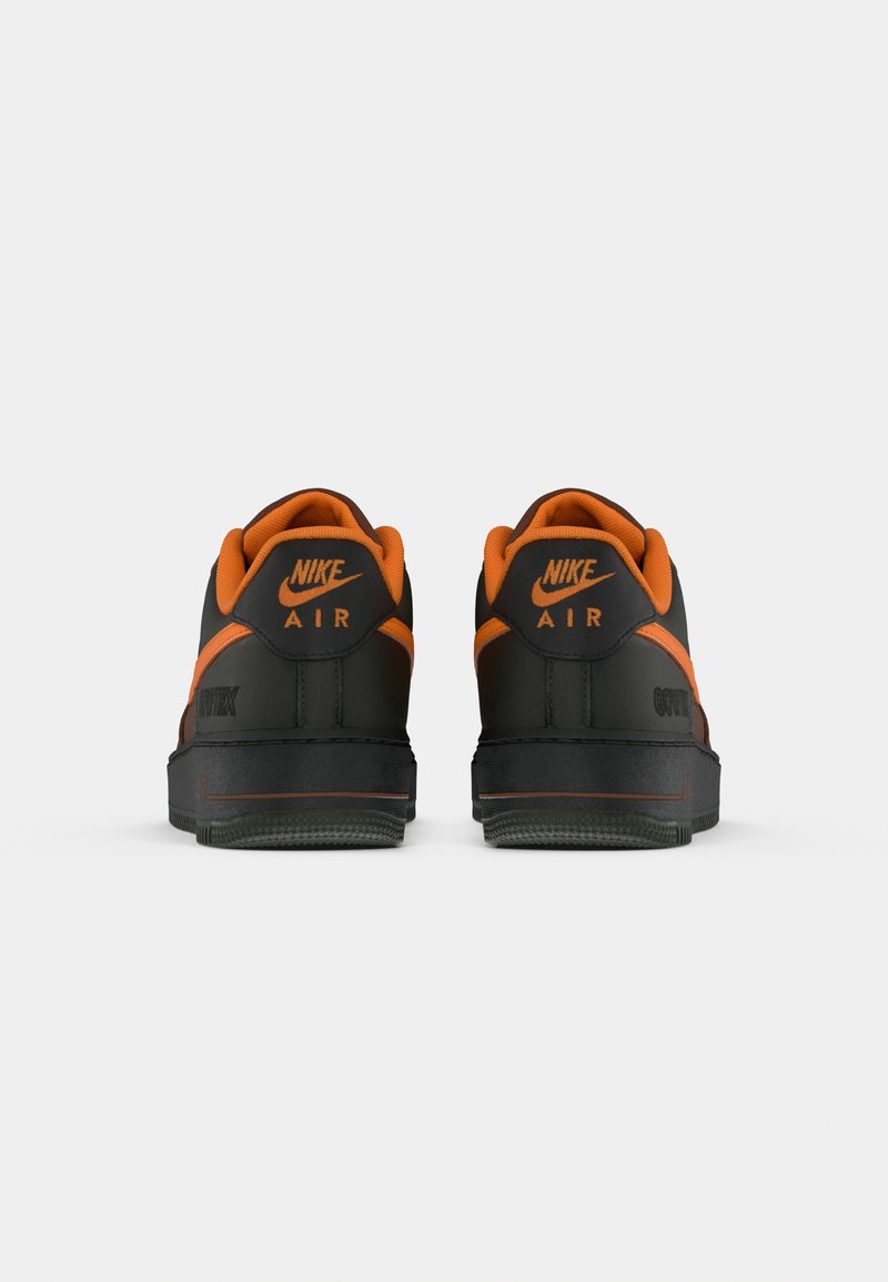 Baskets Nike Air avec un dessus noir et des accents orange, et une semelle texturée. Le talon affiche le logo Nike et le nom du modèle.