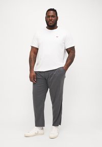 Fehér, crew-neck póló piros logóval, szürke csíkos nadrággal és fehér sportcipővel. Simára szabott anyag, laza fazon, hétköznapi dizájn.