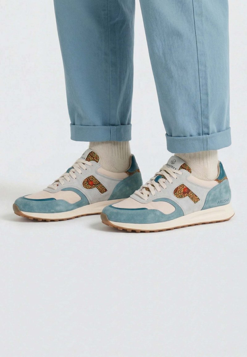 Personne portant un pantalon bleu clair retroussé, des chaussettes crème et des baskets bleu clair et beige avec des détails à motifs et des semelles beiges.