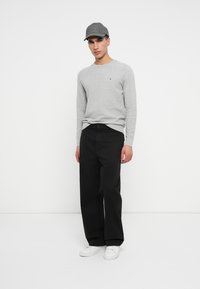 Γκρι ριχτό πουλόβερ, μαύρο παντελόνι σε φαρδιά γραμμή και γκρι καπέλο. Λευκά αθλητικά παπούτσια ολοκληρώνουν την εμφάνιση. Χαλαρός σχεδιασμός με άνετη εφαρμογή.