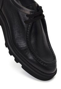 Zwarte leren schoen met een gladde afwerking, ronde neus en vetersluiting; heeft een dikke rubberen zool met een gestructureerd patroon.