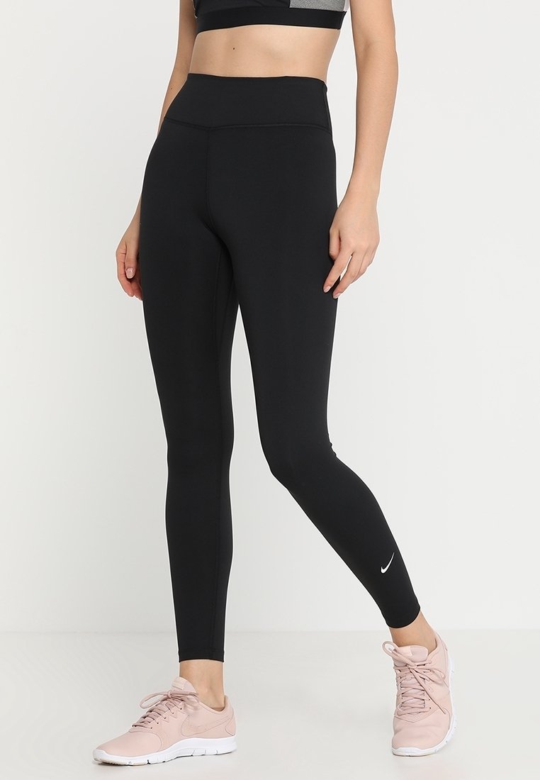 Leggings de sport noirs taille haute, à la texture lisse et un petit logo blanc sur le bas de la jambe, assortis à des baskets rose clair.