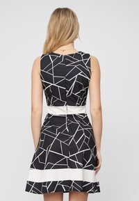Robe noire avec un motif géométrique blanc, sans manches, corps ajusté et jupe évasée, dotée d'une taille contrastante blanche.