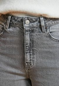 Graue Jeans aus Denim mit einer subtilen Textur, ausgestattet mit einem Knopfverschluss vorne, Gürtelschlaufen und klassischem Fünf-Taschen-Design.