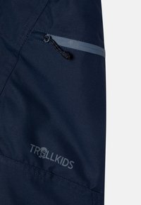 Temno modra vodoodporna tkanina z žepom na zadrgo in črno vrvico; na dnu ima sivo logotip "TROLLKIDS".
