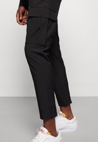 Svarta cargo-byxor med en smal passform, med sidfickor, en något skrynklig textur och i kombination med vita sneakers.