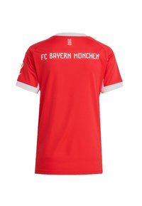 Punainen urheilupaita, jossa on valkoisia yksityiskohtia, lyhyet hihat ja kaulus. "FC BAYERN MÜNCHEN" on painettu selkäpuolelle valkoisilla isoilla kirjaimilla.