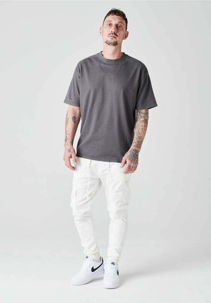 T-shirt en coton gris à manches courtes, assortie à un pantalon cargo blanc avec des poches latérales, et des baskets blanches avec des accents noirs.