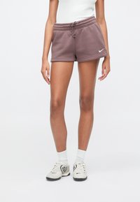 Γυναίκα που φοράει ροζ-μωβ σορτς Nike, λευκές ριμπ κάλτσες και λευκά αθλητικά παπούτσια με μαύρα σχέδια καρδιάς σε λευκό φόντο.