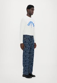 Long-sleeve white shirt with blue "ICECREAM" print; denim pants featuring repeated blue "ICECREAM" text pattern; black shoes.