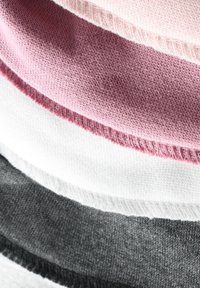 Pièces de tissu superposées en rose, rose clair, blanc et gris foncé. Texture tricotée avec bords côtelés. Tissu doux, nuances variées visibles.