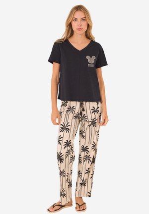 Zwarte T-shirt met korte mouwen en V-hals met witte Mickey Mouse graphic, gecombineerd met beige broek met zwart palmbomenprint. Model draagt slippers.