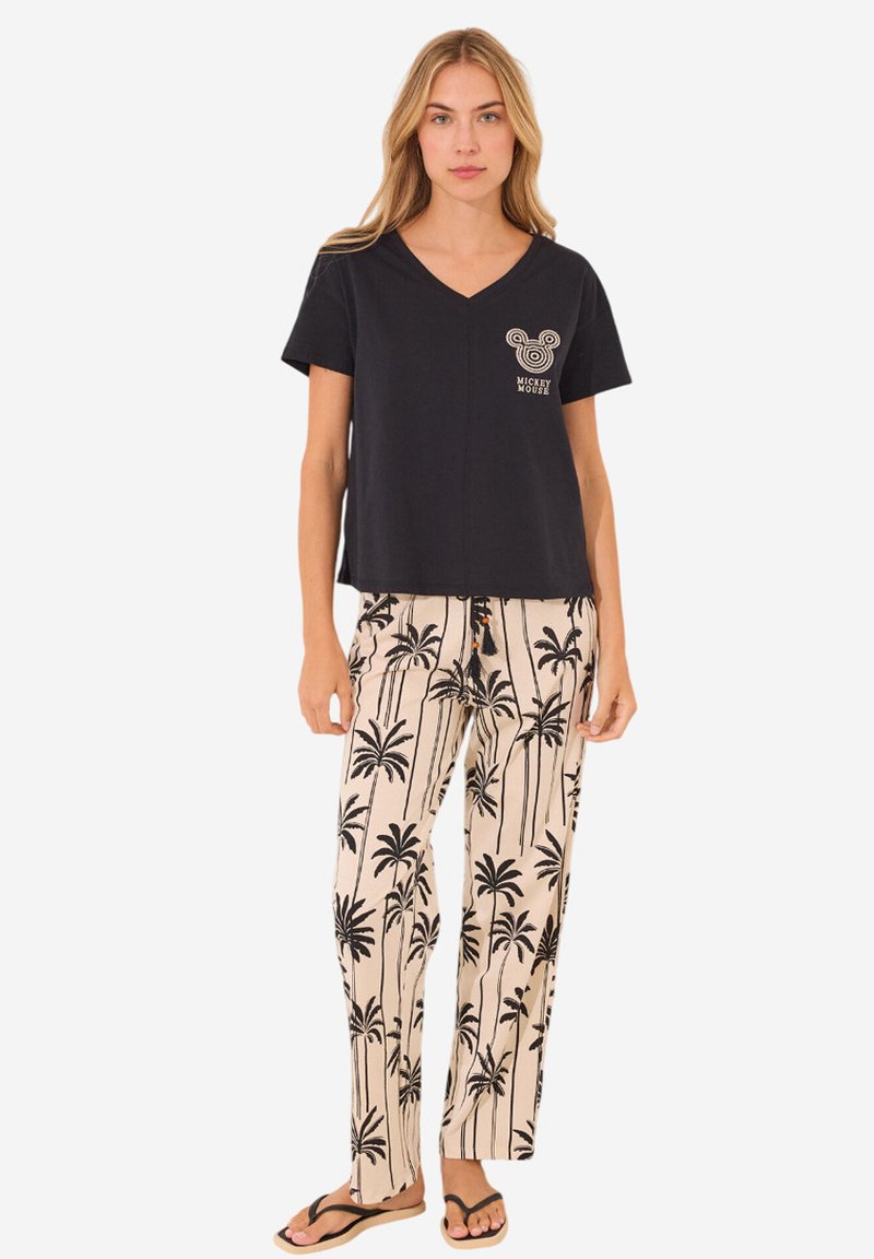 Zwarte T-shirt met korte mouwen en V-hals met witte Mickey Mouse graphic, gecombineerd met beige broek met zwart palmbomenprint. Model draagt slippers.