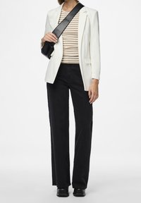 Bílý blazer přes béžový a hnědý pruhovaný top, doplněný černými širokými džíny a černými botami. Obsahuje černou křížovou tašku.