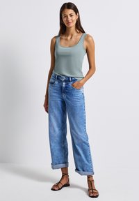 Ljusgrön linne med rundad halsringning, matchat med ljusblå vida jeans som är uppvikta vid fållarna, och svarta platta sandaler.