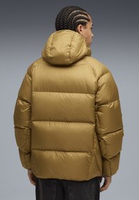 Kaki puffjacka med huva, med quiltade sektioner och en mjuk textur. Designen är oversized med en avslappnad passform.