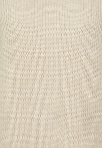 Pull beige tricoté présentant un motif texturé. Le tissu est épais avec un design côtelé, offrant chaleur et douceur au toucher.