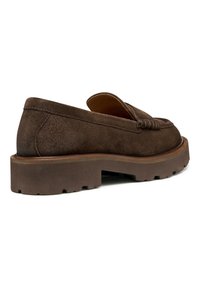Bruine suede instappers met een ronde neus, een lage, dikke zool en decoratieve stiksels op de bovenkant. Zichtbare textuur en gladde accenten.