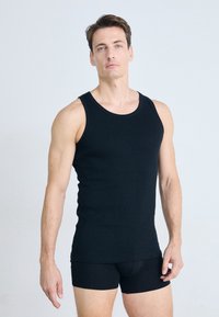 Débardeur en coton noir avec un col rond, une coupe sans manches et ajustée. Le modèle porte également un short noir. Texture simple et lisse.