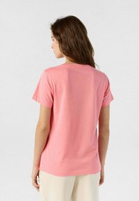 Camiseta de algodón rosa con mangas cortas y cuello redondo, que presenta una textura suave y un ajuste relajado. El fondo es blanco.