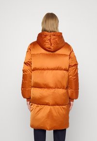 Rostfärgad puffjacka med huva, med quiltat mönster, stora sydda paneler och en slät, glänsande yta.