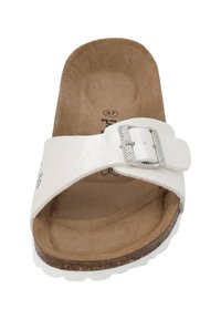 Chancla blanca con interior texturizado, una correa ancha con una hebilla decorativa de plata y una suela de corcho marrón acolchada.