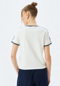Hvid T-shirt med korte ærmer og mørkegrå kant omkring kraven og ærmerne. Glat bomuldsstof med en afslappet pasform.