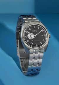 Reloj automático de acero inoxidable con esfera negra, subesfera blanca, agujas y números plateados. Cuenta con una pulsera de metal y una pantalla de fecha.