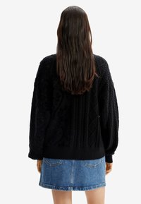 Černý pletený svetr s texturovanými vzory copánků, kombinovaný s modrou džínovou sukní. Svetr má volný střih a žebrované manžety.