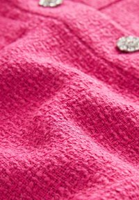 Tissu rose texturé avec un motif tissé, comportant des boutons décoratifs brillants ; aspect doux et pelucheux.