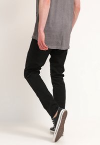 Pantalones negros ajustados hechos de una mezcla de algodón, que presentan una textura suave y un clásico diseño de cinco bolsillos. Combinados con zapatillas de lona negras.