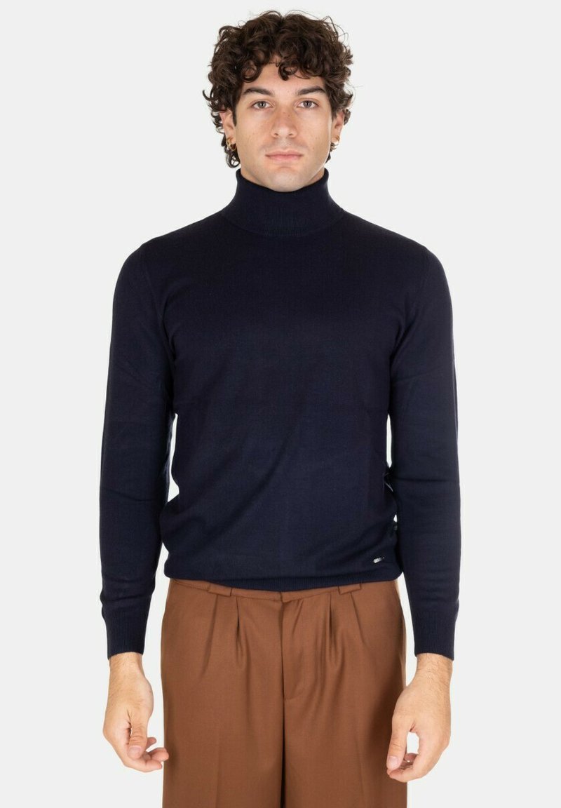 Maglione turtleneck navy in morbido tessuto, caratterizzato da un design aderente con maniche lunghe e polsini a coste. Abbinato a pantaloni marroni.