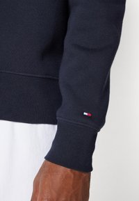 Felpa blu navy con polsini a coste e un piccolo logo rosso, bianco e blu sulla manica. Realizzata in tessuto morbido e strutturato.