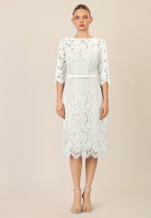 Lace dress in white with three-quarter sleeves, fitted waist, and scalloped hem. Includes a matching belt; intricate floral pattern throughout.
