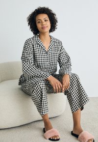 Svart-vitt rutig pyjamas-set i ett lätt material, bestående av en knappad skjorta och löst sittande byxor, kombinerat med rosa päls-slapper.