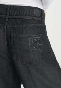 Zwarte denim jeans met een gestikt achterzakontwerp, textuurstof en een gelabelde tailleband. Minimalistische esthetiek met strakke lijnen.