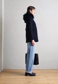 Tamsiai mėlyna striukė su kailiniu gobtuvu, šviesiai mėlyni tiesūs džinsai, juoda rankinė ir juodi aukštakulniai bateliai, esantys neutralioje fone.