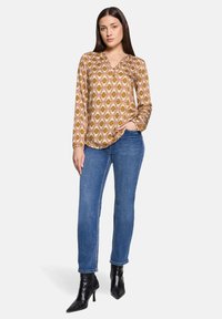 Blusa a maniche lunghe con motivo in tonalità calde e scollo a V. Abbinata a jeans blu e stivaletti neri a punta. Tessuto liscio.