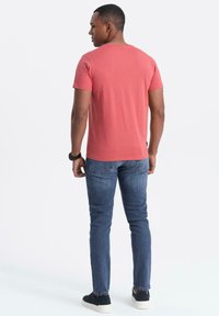 Röd bomullströja med korta ärmar och rundad halsringning, kombinerad med blå slim fit-jeans och svarta sneakers. Modellen sedd bakifrån.