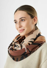 Foulard marron et beige à motifs en tissu doux, drapé autour du cou. Présente des formes abstraites et une texture lisse.
