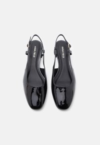 Μαύρες πατίνες από λουστρίνι, με στρογγυλή μύτη, λουράκι στον αστράγαλο και διακριτική σήμανση στη σόλα. Λείο, γυαλιστερό φινίρισμα.