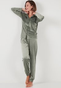 Conjunto de loungewear de terciopelo en un suave tono verde, que incluye una blusa de botones de manga larga y unos pantalones ajustados a juego con un ajuste cómodo.