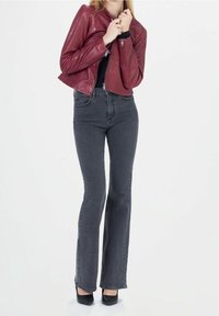 Punainen nahasta valmistettu lyhyt takki, jossa on vetoketju, yhdistettynä korkeavyötäröisiin tummanharmaisiin flarefarkkuihin. Mallilla on jalassaan mustat korkokengät.