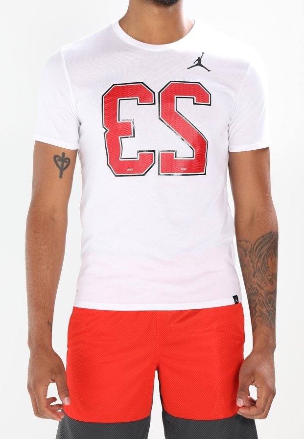 Vit T-shirt i bomull med röda grafiska bokstäver "ES" och en svart logotyp på bröstet. Buren med röda sportshorts med nätstruktur.