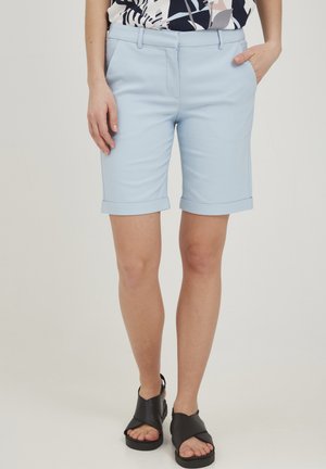 Light blue tailored shorts with rolled cuffs and side pockets, made from smooth fabric. Paired with black strappy sandals.