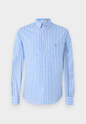 Kék és fehér kockás gombos ing hosszú ujjakkal, gallérral és mellzsebbel. Az anyag simának és könnyűnek tűnik.