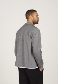 Grijze, gemarmerde jas met een kraag en lange mouwen, met knopenaccenten op de manchetten en zijzakken. Minimalistisch ontwerp.